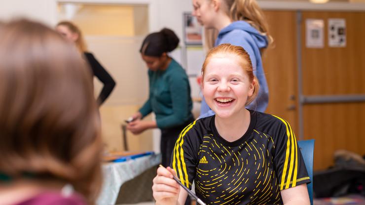 Jente som smiler stort mens hun sitter ved et bord og maler